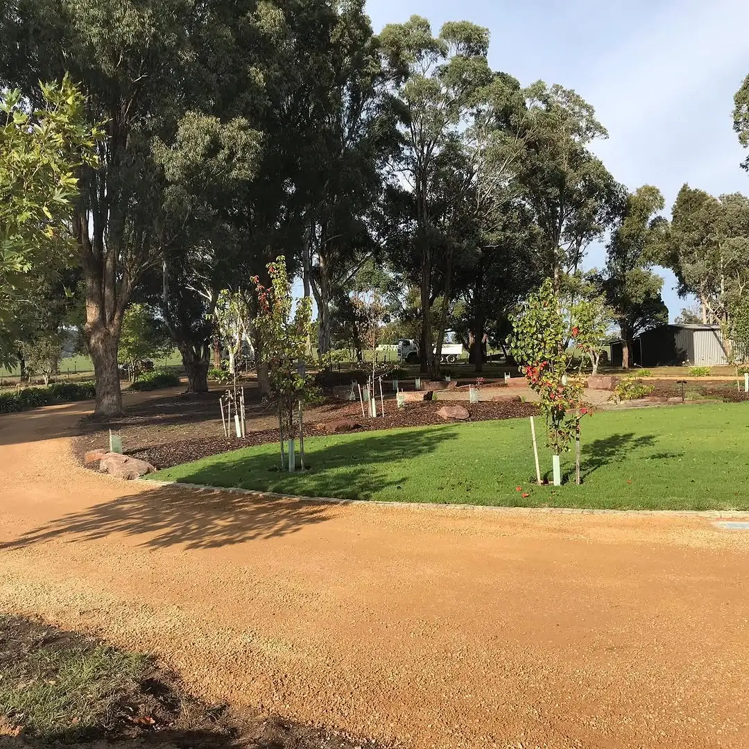 Edge of the Coldstream gravel driveway meeting fresh lawn and a planted garden bed with young trees
