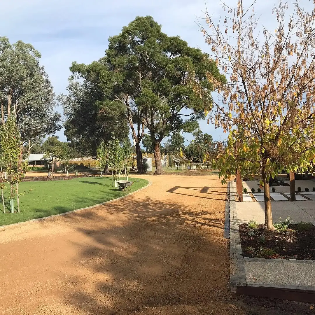 Finished gold gravel driveway at Coldstream curving past new lawn, young trees and a paved garden area