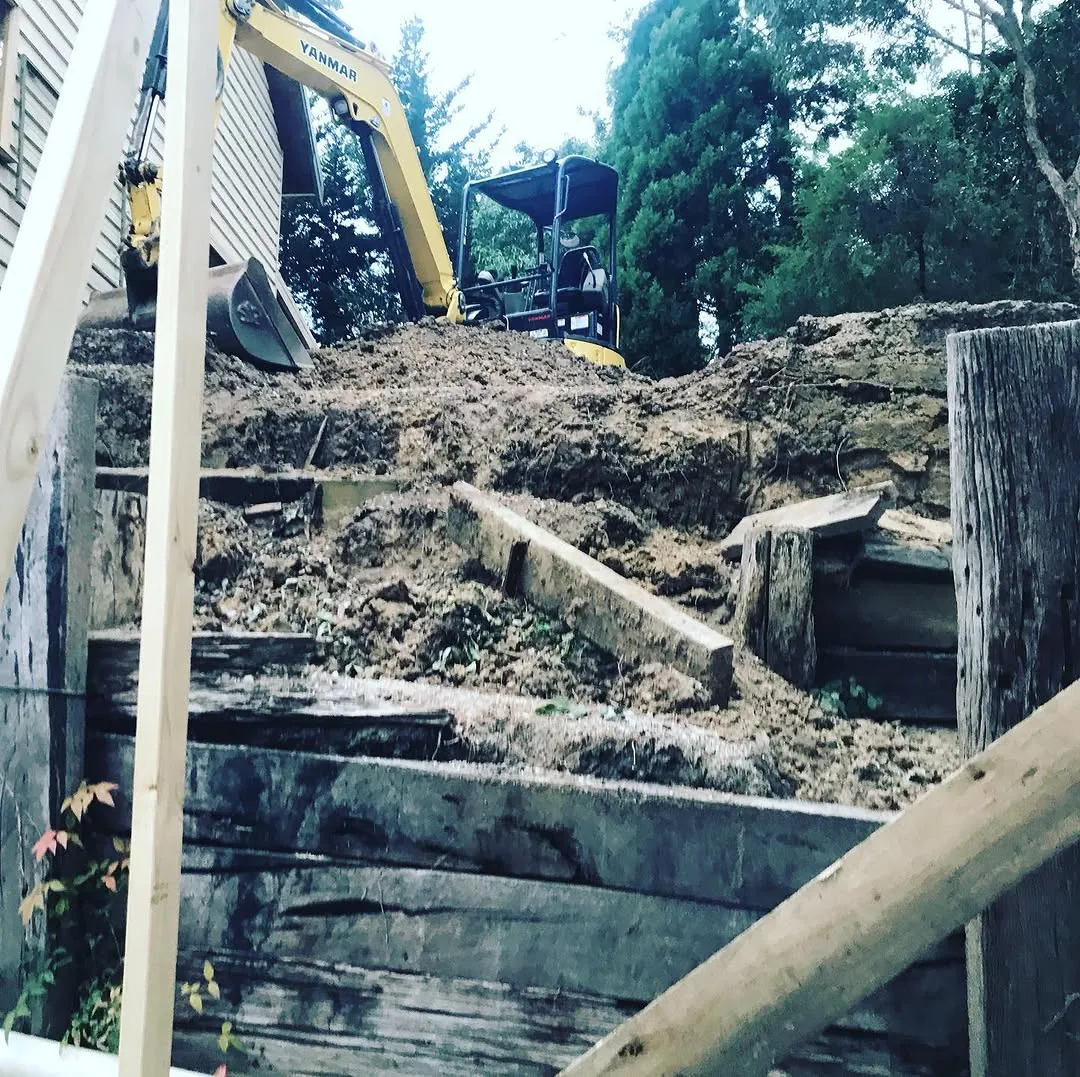Looking up the Healesville cut from below, excavator at the top of the face above old timber sleeper retaining